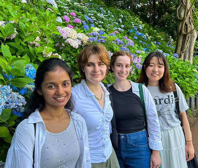 Four Students standing in front of colorful hydrangea flowers in a garden.